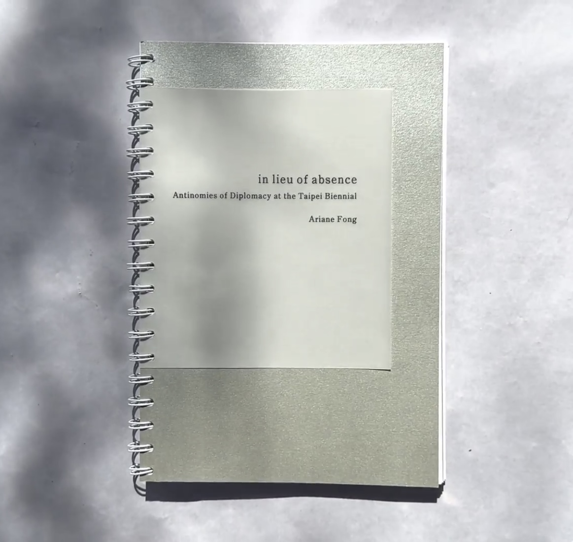 a wirebound book with a silver ccover that reads 'in lieu of absence'